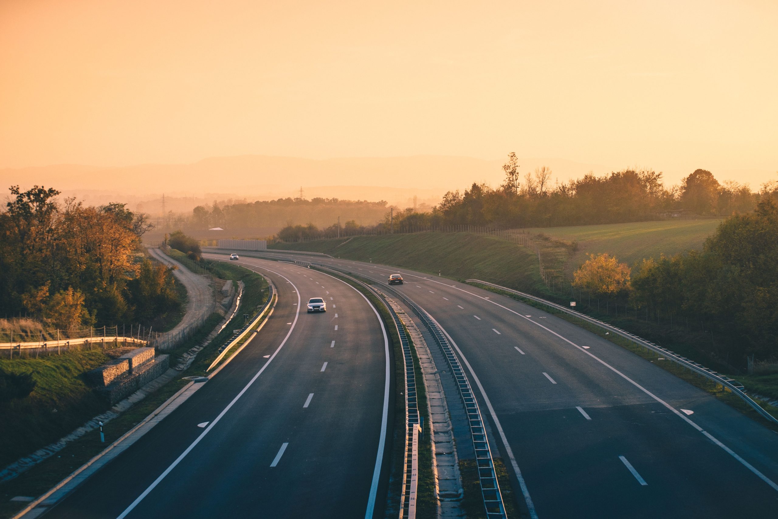 Aerial view of a truck on an empty highway with trees and hills in the background