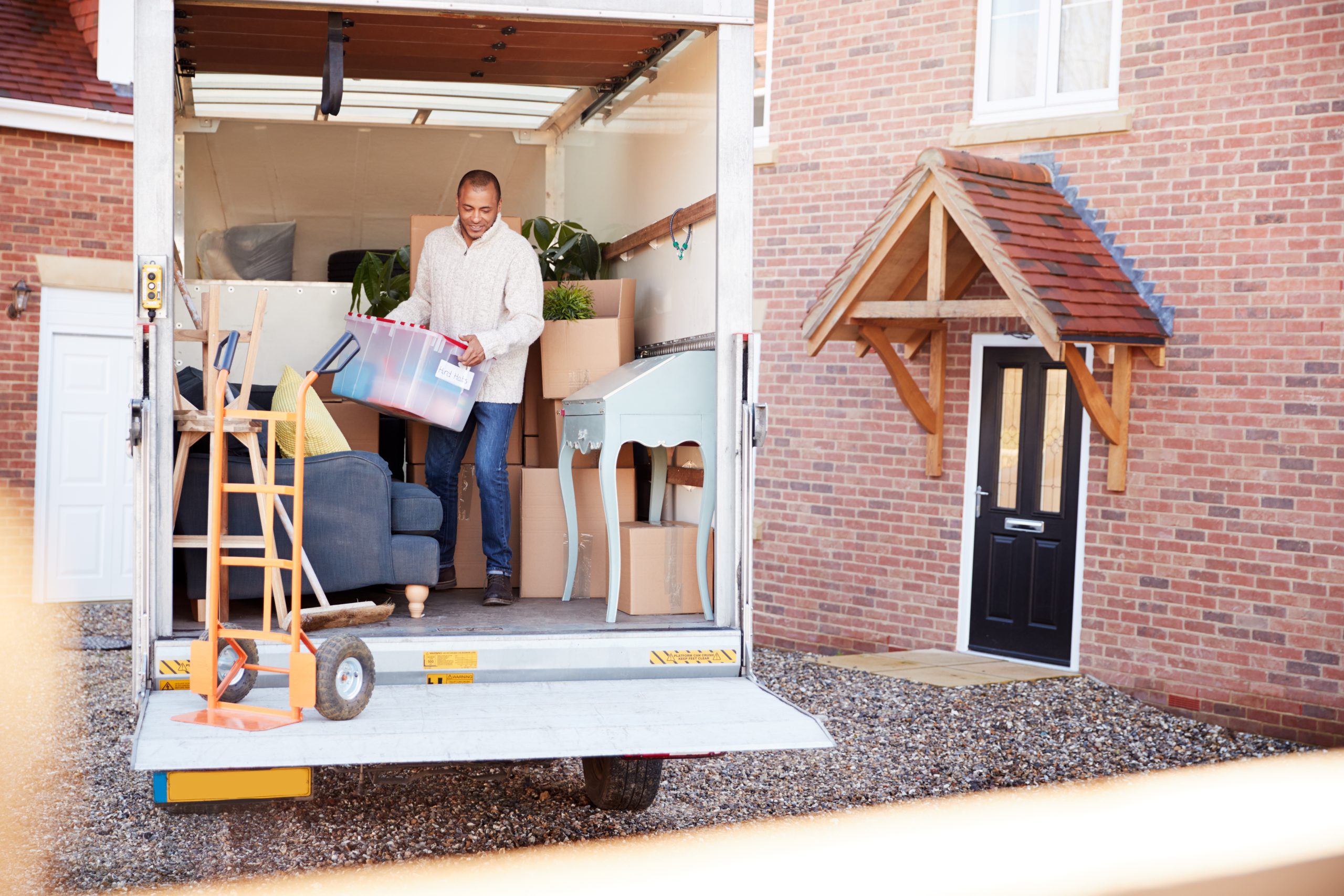 Man Unloading Furniture From Removal Truck Outside New Home On Moving Day